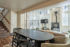 A spacious living area with a large table, comfortable seating, a fireplace, and a staircase. - Stunning Sunlit & Spacious-1BR/2BTH+Loft (Mammoth Lakes)