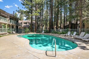 A swimming pool with a curved edge, surrounded by lounge chairs and a fence. - Stunning Sunlit & Spacious-1BR/2BTH+Loft (Mammoth Lakes)