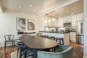 A modern kitchen with stainless steel appliances, a dining area with a large table and chairs, and artwork on the walls. - Stunning Sunlit & Spacious-1BR/2BTH+Loft (Mammoth Lakes)