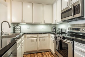 A modern kitchen with white cabinetry, stainless steel appliances, and a black countertop. - Stunning Sunlit & Spacious-1BR/2BTH+Loft (Mammoth Lakes)