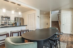 A modern kitchen with stainless steel appliances, a dining area with a large table and chairs, and a staircase leading to another level. - Stunning Sunlit & Spacious-1BR/2BTH+Loft (Mammoth Lakes)