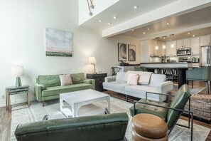 A modern living room with a sofa, coffee table, and ottoman. There is a kitchen area with cabinets and appliances. - Stunning Sunlit & Spacious-1BR/2BTH+Loft (Mammoth Lakes)