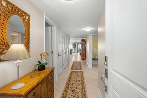 A hallway with a wooden dresser, a mirror, and a floral rug. - Kings Crown 318 3 Bedroom Condo (Sanibel)