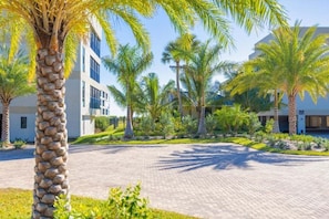 A paved courtyard with palm trees and a modern building with large windows. - Kings Crown 318 3 Bedroom Condo (Sanibel)