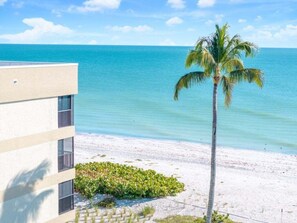 A beachfront hotel with a palm tree, clear blue water, and a sandy beach. - Kings Crown 318 3 Bedroom Condo (Sanibel)