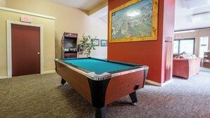 A pool table in a room with a carpeted floor, a door with an exit sign, a framed painting on the wall, and a red couch. - Adventure Basecamp! 1BR + Loft Close to Village (Mammoth Lakes)