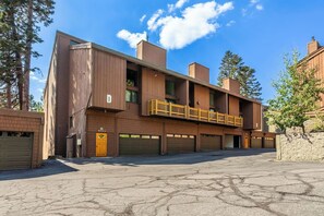 A multi-story building with a brick facade, multiple garage doors, and a wooden balcony. - Adventure Basecamp! 1BR + Loft Close to Village (Mammoth Lakes)