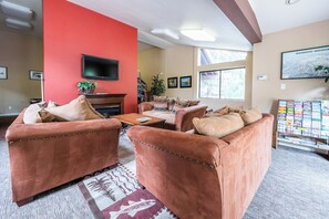 Ein Wohnzimmer mit roter Akzentwand, Ledersofas, einem Kamin, einem Flachbildfernseher und einem großen Fenster.