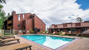 A pool area with lounge chairs, a brick building, and a clear sky. - Adventure Basecamp! 1BR + Loft Close to Village (Mammoth Lakes)