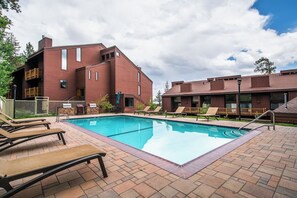 A pool area with lounge chairs, a brick building, and a clear sky. - Adventure Basecamp! 1BR + Loft Close to Village (Mammoth Lakes)