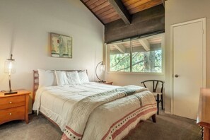 Um quarto com cama, mesa de cabeceira, abajur, janela e uma cadeira.