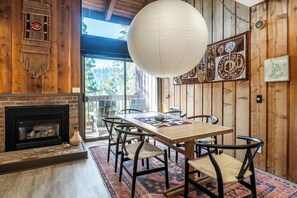 Interior em madeira com lareira, mesa de jantar com cadeiras e um lustre grande.