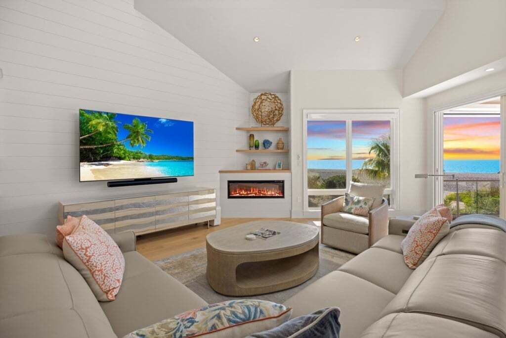 A modern living room with a flat-screen TV, a fireplace, a sofa, and a view of the ocean.