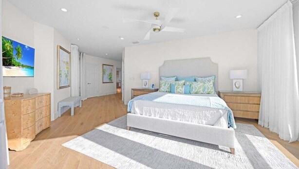 A spacious bedroom with a large bed, a ceiling fan, and a view of a beach through the window. - Angel's View 4 Bedroom Home (Captiva)