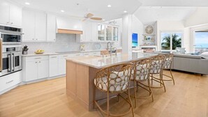 A modern kitchen with white cabinetry, a central island with bar stools, and a view of the ocean. - Angel's View 4 Bedroom Home (Captiva)
