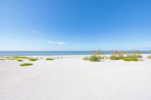 A sandy beach with sparse vegetation and a clear blue sky. - Seashells Unit 30 - Driftwood Dreams 2 Bedroom Condo (Sanibel)