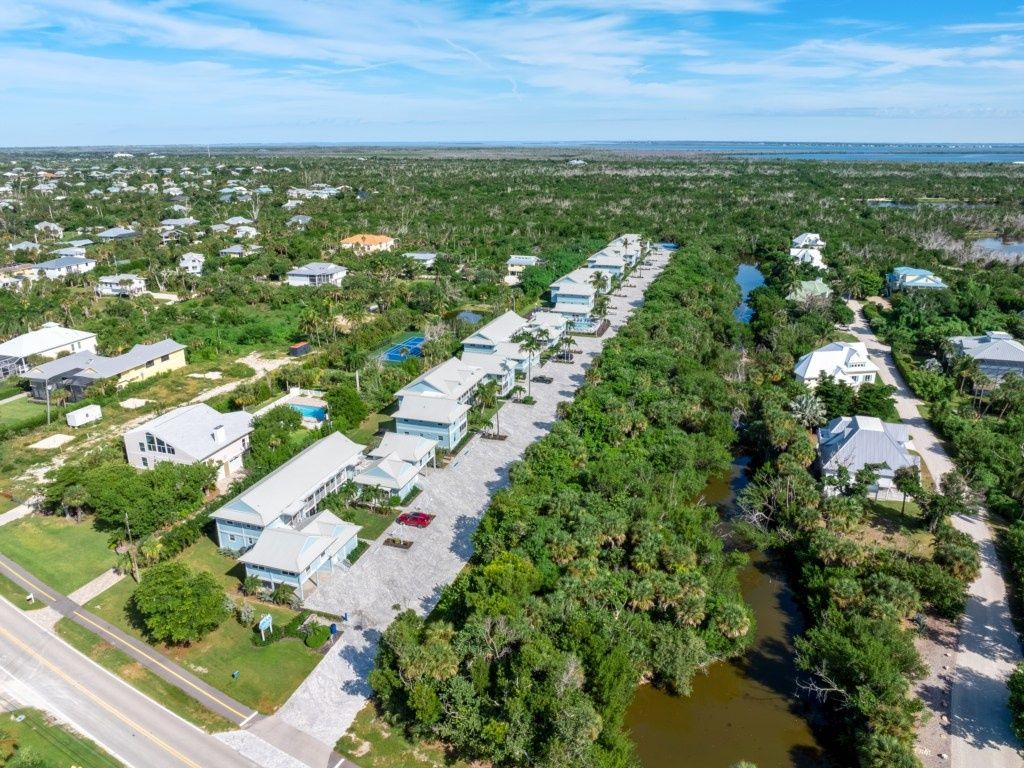 An aerial view of a residential area with houses aligned along a waterway, surrounded by dense vegetation.