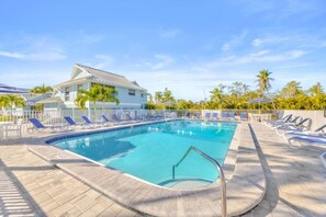 A swimming pool with lounge chairs, a building with a sloped roof, and palm trees. - Seashells Unit 30 - Driftwood Dreams 2 Bedroom Condo (Sanibel)