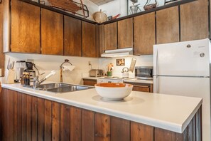 Une cuisine avec des meubles en bois, un plan de travail blanc, un évier, un grille-pain, un four à micro-ondes et un réfrigérateur blanc.