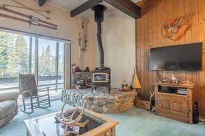 Un salon chaleureux avec une cheminée en pierre, un téléviseur fixé au mur et une vue sur l’extérieur.