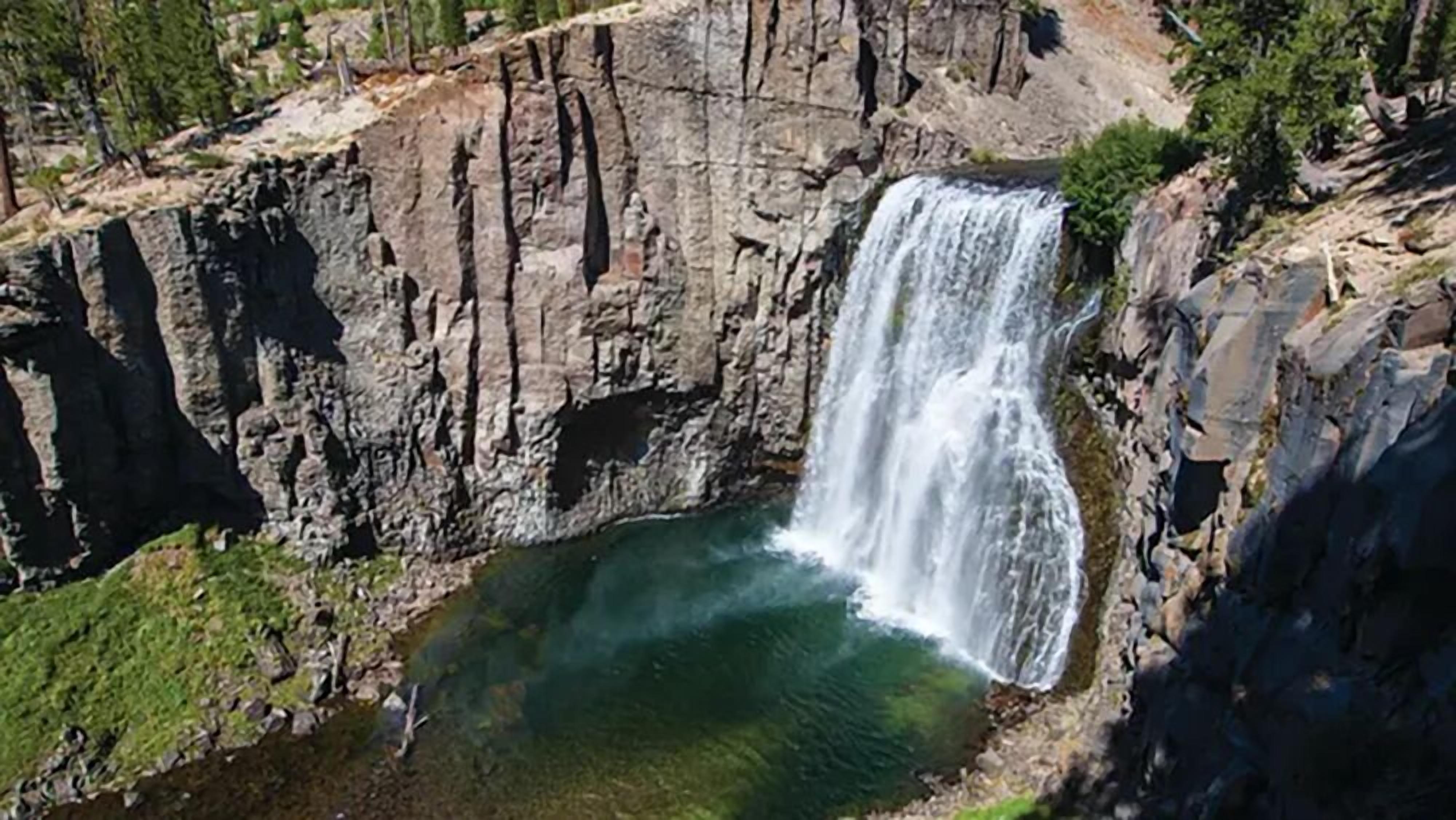 Een waterval stort neer op een rotswand in een poel, omringd door begroeiing.