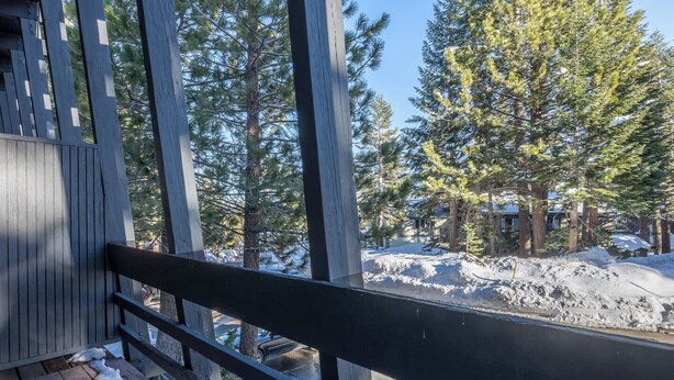 Eine Holzterrasse mit Geländer, mit Blick auf eine verschneite Landschaft mit Bäumen und einem Gebäude im Hintergrund.