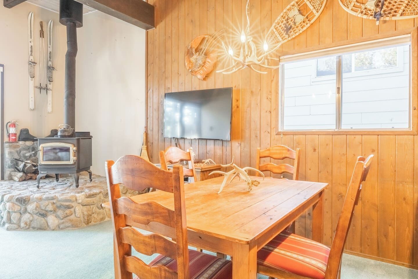 A wooden interior with a stone fireplace, a television mounted on the wall, and a dining table with chairs.