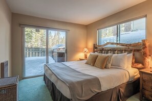 Une chambre avec un grand lit, une tête de lit en bois, une table de chevet avec une lampe, et une vue sur un espace extérieur enneigé grâce à une porte coulissante.
