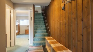 Eine Treppe mit einer Schachbrettbank, Holzwänden und Blick in einen Raum mit Bett und Kommode.