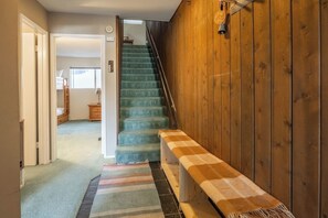 Eine Treppe mit einer Schachbrettbank, Holzwänden und Blick in einen Raum mit Bett und Kommode.