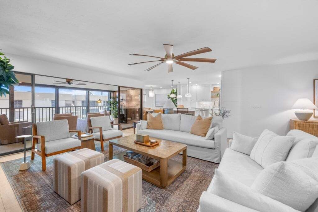 A modern living room with a sofa, armchairs, ottomans, a coffee table, and a ceiling fan.