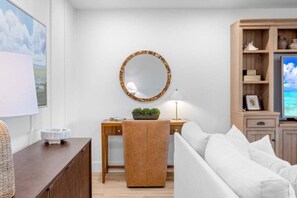 A living room with a sofa, a coffee table, a side table with a lamp, a decorative mirror, and a television on a wooden cabinet. - Kings Crown Unit 305 3 Bedroom Condo (Sanibel)