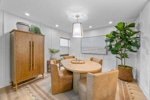 A modern dining area with a wooden table and chairs, a cabinet, and a hanging light fixture. - Kings Crown Unit 305 3 Bedroom Condo (Sanibel)