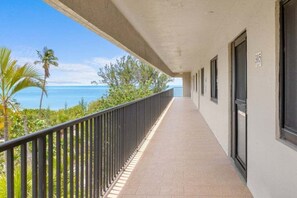 A corridor with a view of the ocean, palm trees, and a balcony with a railing. - Kings Crown Unit 305 3 Bedroom Condo (Sanibel)