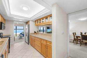 A modern kitchen with wooden cabinets, a large island, and a view to the outside. - Kings Crown Unit 217 2 Bedroom Condo (Sanibel)