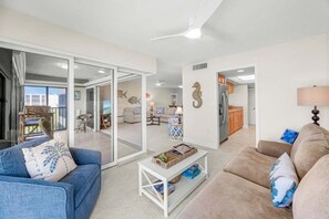 A spacious living area with a blue sofa, a beige sofa, a white coffee table, and a kitchen in the background. - Kings Crown Unit 217 2 Bedroom Condo (Sanibel)