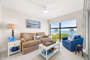 A living room with a sofa, a coffee table, a lamp, and a painting. - Kings Crown Unit 217 2 Bedroom Condo (Sanibel)