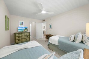 A bedroom with two beds, a dresser, a ceiling fan, and a door leading to another room. - Kings Crown Unit 217 2 Bedroom Condo (Sanibel)