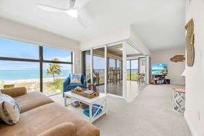 A spacious living area with a large window overlooking a beach, a comfortable seating area, and a view of the ocean. - Kings Crown Unit 217 2 Bedroom Condo (Sanibel)