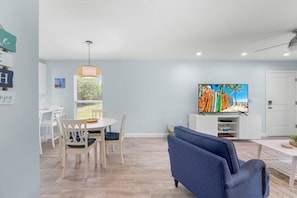 A modern living room with a dining area, a television, and a large window. - Seashells Unit 32 2 Bedroom Condo (Sanibel)