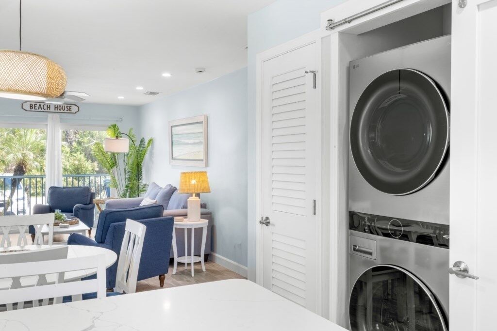 Une pièce comprenant une table à manger, des chaises, un canapé, une lampe, un lave-linge et une porte portant l’inscription « MAISON DE PLAGE ».