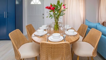 A dining area with a round table set for six, surrounded by wicker chairs, a vase with flowers, and a blue cabinet in the background.