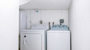 Uma lavanderia com duas máquinas de lavar e secar de carregamento frontal, um aquecedor de água e uma tomada elétrica na parede.