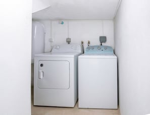 Ein Waschraum mit zwei Waschmaschinen und Trocknern, einem Warmwasserbereiter und einer an der Wand montierten Steckdose.