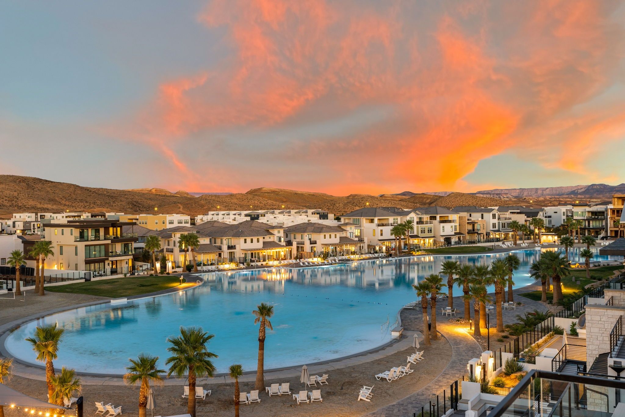 A resort with a large swimming pool, multiple buildings, and a desert landscape in the background.