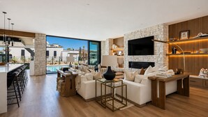 Amplia sala de estar con pared de piedra, televisor de pantalla plana y una piscina visible a través de amplios ventanales.