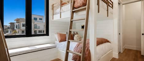 A bunk bed room with a window, wooden flooring, and a view of buildings outside.