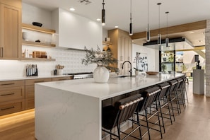 A modern kitchen with a large island, bar stools, and pendant lighting. - Paradise Palace 8 Bedroom Home (St. George)