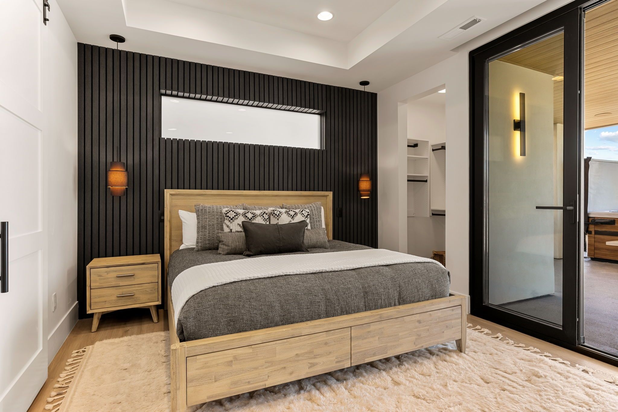 A modern bedroom with a bed, bedside tables, a large mirror, and a sliding glass door leading to a balcony.