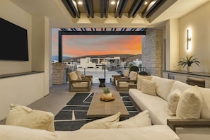 A modern living room with a sofa set, a coffee table, and a view of a sunset through a large window. - Paradise Palace 8 Bedroom Home (St. George)